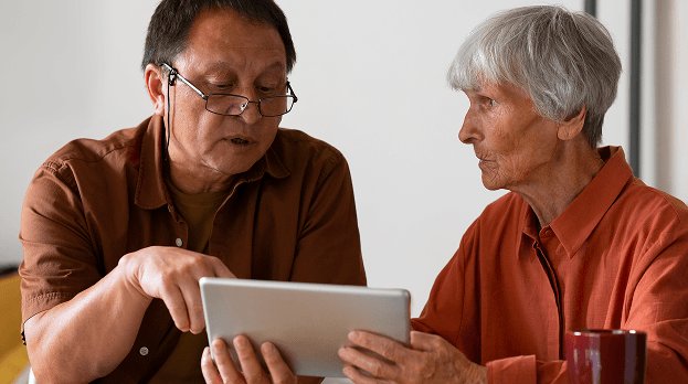 Two older adults looking at a tablet together and discussing.