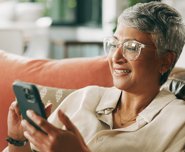 An older woman with glasses smiling and looking at her phone.