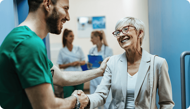 A healthcare worker shaking the hand of an older female patient in a medical environment.